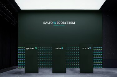 Auf moosgrünem Hintergrund stehen drei Säulen mit der Aufschrift "Salto W-Ecosystems". Die erste trägt das Logo von Gantner, die zweite das von Salto und die dritte das von Vintia. 
