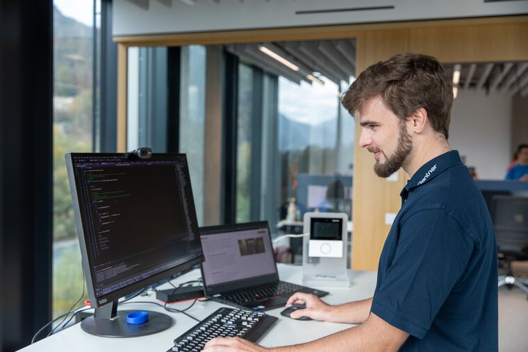 Ein junger Mann mit dunklen Haaren und Bart arbeitet konzentriert an einem Monitor, der mit seinem Laptop verbunden ist.