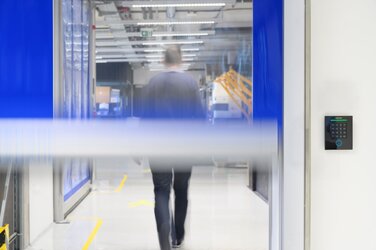 Ein Mann passiert einen Durchgang, der mit einem Gantner-Sicherheitssystem ausgestattet ist.  Hinter dem Mann schließt sich gerade eine Schranke.