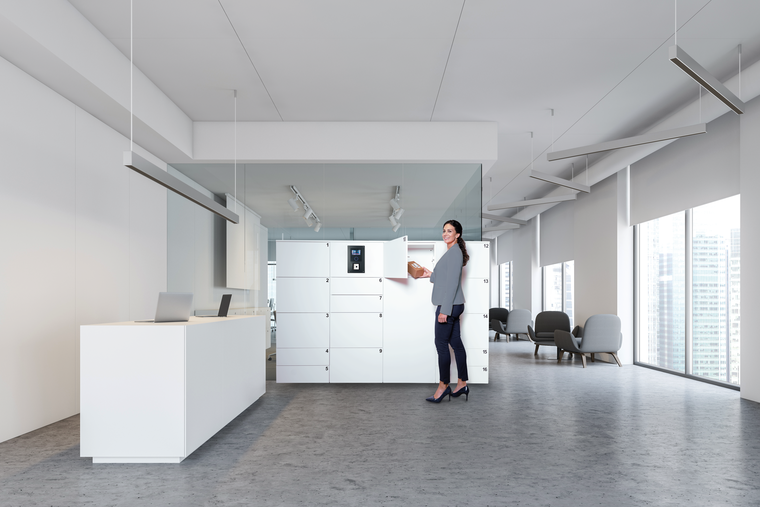 Eine Frau im roten Blazer bedient das Bedienfeld einer Schließfachanlage, um ein Fach mit einem Paket zu beladen.