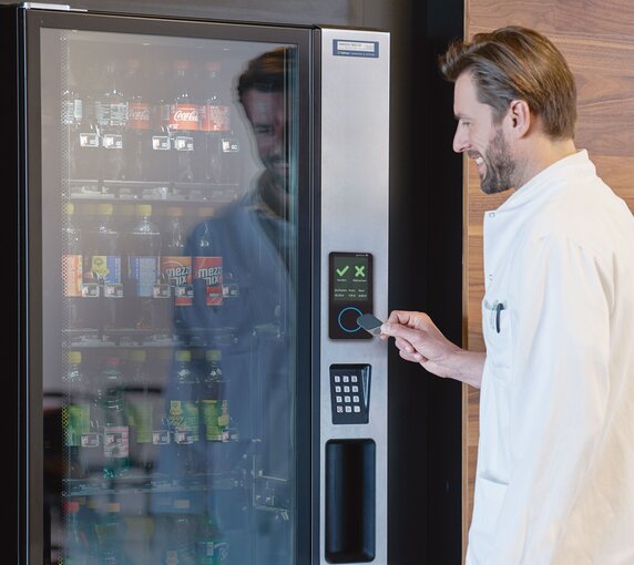Ein Mann hält einen speziellen Chip an einen Sensor von Gantner, der in einen Getränkeautomaten integriert ist, um ein kühles Getränk zu erhalten.