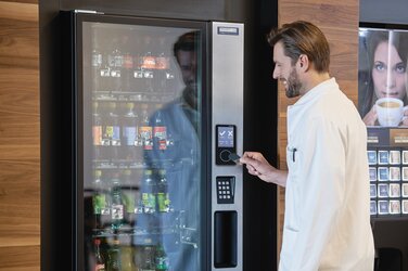 Ein Mann hält einen speziellen Chip an einen Sensor von Gantner, der in einen Getränkeautomaten integriert ist, um ein kühles Getränk zu erhalten.