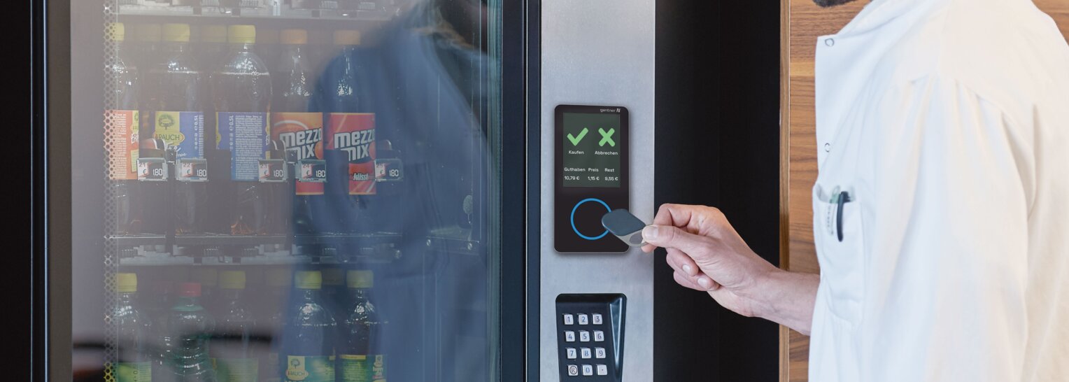 Ein Mann hält einen speziellen Chip an einen Sensor von Gantner, der in einen Getränkeautomaten integriert ist, um ein kühles Getränk zu erhalten.