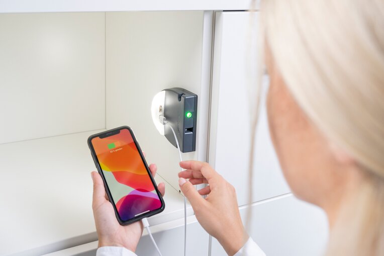 Eine Frau lädt ihr Smartphone an den integrierten Ladestationen der Gantner Schließsysteme auf.