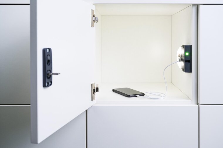 In einem geöffneten, weißen Schließfach wird gerade ein Smartphone über die integrierte Ladestation der Gantner Spindlösungen aufgeladen.